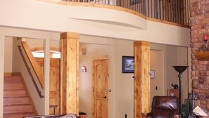 A spacious living area with a wooden ceiling, a stone accent wall, a leather sofa, and a staircase leading to an upper level. - RIVER FRONT front property with Hot Tub! Bring the dogs! (Bend)