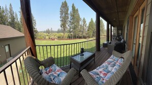 A covered outdoor deck with wicker furniture and a glass table, overlooking a grassy yard and trees. - RIVER FRONT front property with Hot Tub! Bring the dogs! (Bend)