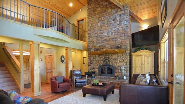 A spacious living area with a stone fireplace, a wooden staircase, and a cozy seating arrangement. - RIVER FRONT front property with Hot Tub! Bring the dogs! (Bend)