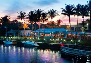 A waterfront restaurant with a view of the water, docked boats, and palm trees.