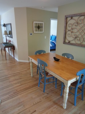 A dining area with a wooden table and blue chairs, a small side table with a lamp, and a decorative wall piece.
