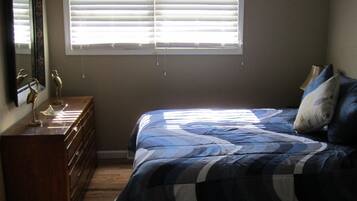A bedroom with a bed, dresser, ceiling fan, and window with blinds.
