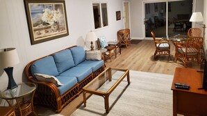 A living room with a blue sofa, wicker chairs, a glass coffee table, and a dining table with chairs. - BEST VALUE!! SPACIOUS Home! Short Walk to Beach! Many Amenities!! Great Reviews! (Rehoboth Beach)