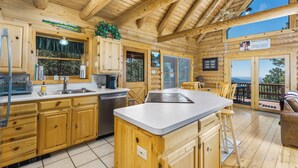 A wooden cabin with a kitchen featuring wooden cabinets, a sink, a stove, and a bar area with stools.