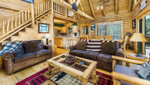 A wooden cabin interior with a staircase, two sofas, a coffee table, and a dining area.