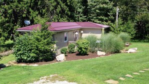 A small house with a red roof, surrounded by a well-maintained garden with various shrubs and a lawn. - Rest, Relaxation, & Quick Access to Ohiopyle Await (Ohiopyle)