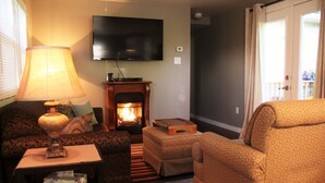 A living room with a fireplace, a television mounted on the wall, and a patterned armchair. - Rest, Relaxation, & Quick Access to Ohiopyle Await (Ohiopyle)