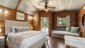 Camera da letto in un accogliente cottage di legno, con un letto grande, una panca, un divano e una ventola a soffitto.