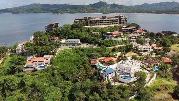 Un resort costero con varias edificaciones, incluyendo un hotel grande de varios pisos y una piscina.