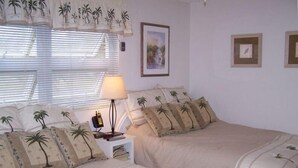 A bedroom with two beds, each with palm tree patterned bedding, a bedside lamp, and a framed picture on the wall. - Pass-a-Grille Sunsets Are the Best! (st. pete Beach)