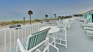 A seaside balcony with white chairs and tables, overlooking a beach and parked cars. - Pass-a-Grille Sunsets Are the Best! (st. pete Beach)