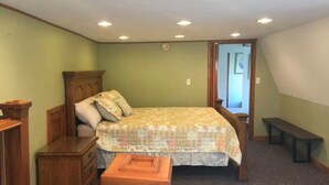 A bedroom with a bed, wooden dresser, bench, and a door leading to another room.