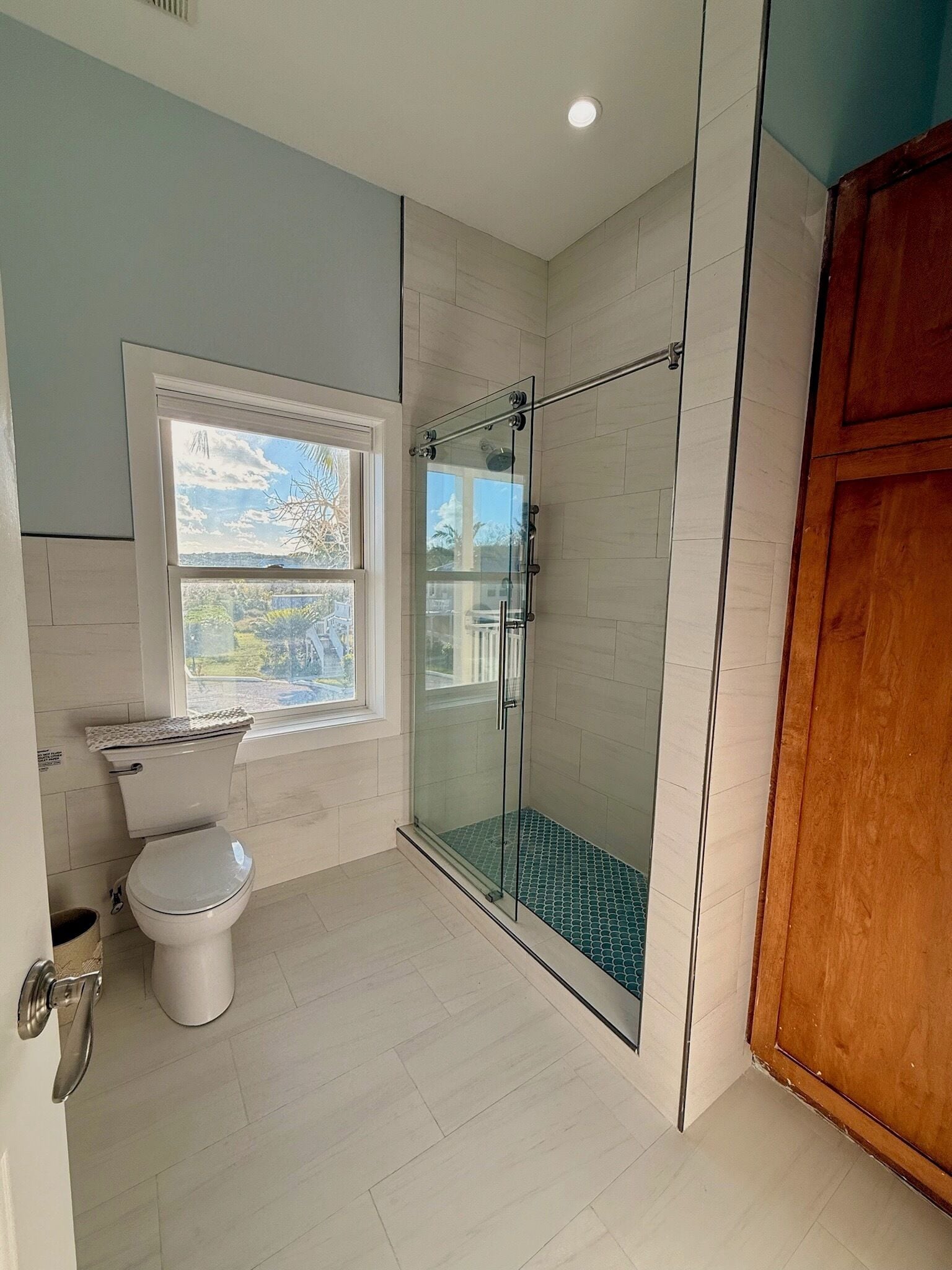 Un baño con inodoro, ducha con mampara de vidrio y ventana con vistas.
