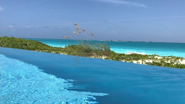Piscina azul cristalina con vista al océano y la vegetación de la playa.