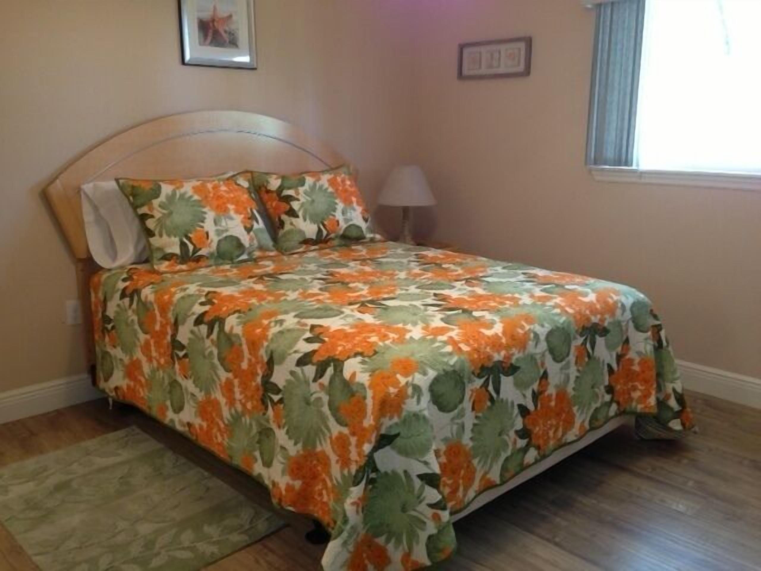 A bedroom with a floral bedspread, a wooden headboard, a bedside lamp, and a small rug.