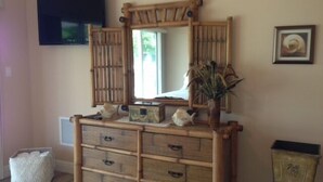 A room with a wooden dresser, a mirror, and a television on the wall.
