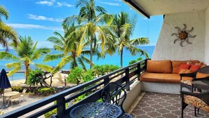 A balcony with a view of the ocean, palm trees, and a sun decoration on the wall. - Kitchen and Bath Remodel! - Ocean Front - Central Air - Featured on Today Show (Kailua-Kona)