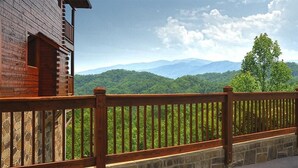 A wooden cabin with a stone foundation and a wooden railing overlooking a mountainous landscape. - Smoky Mountain Dream: Luxury Resort Cabin - New Hot Tub (Sevierville)