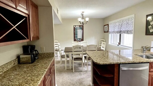 A kitchen with granite countertops, wooden cabinets, a dining area with chairs, and a built-in dishwasher. - Upgraded 3 BR condo on Pinehurst Course 3- walking distance to main club house (Pinehurst)