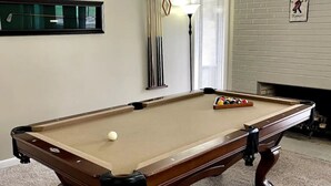 A pool table in a room with a fireplace, a framed welcome sign, and a window with blinds. - Upgraded 3 BR condo on Pinehurst Course 3- walking distance to main club house (Pinehurst)