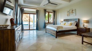 Ein geräumiges Schlafzimmer mit einem großen Bett, einem Deckenventilator und Blick auf einen Pool durch die Glastüren.