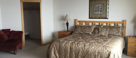 A bedroom with a large bed, a wooden headboard, a nightstand with a lamp, a framed picture on the wall, and a red chair.
