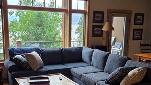 A living room with a sectional sofa, a coffee table, and large windows offering a view of trees and water.