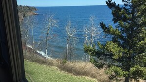 A view of the ocean from a window overlooking a grassy area with trees and a clear sky.