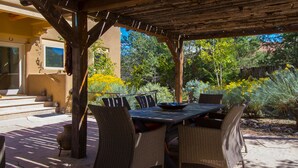 Een terras buiten met een tafel en stoelen, omgeven door een tuin met verschillende planten en bloemen.