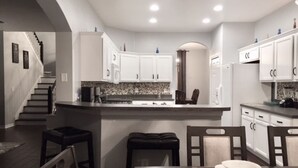 Una cocina moderna con armarios blancos, una isla central y un comedor con mesa y sillas.