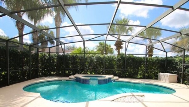 Una piscina techada con jacuzzi, rodeada de palmeras y un cielo despejado.