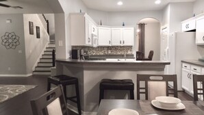 Una cocina moderna con armarios blancos, una isla central y un comedor con mesa y sillas.