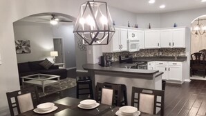 Una cocina moderna con armarios blancos, una isla central y una zona de comedor con una mesa y sillas de madera oscura.