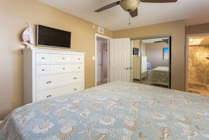 A bedroom with a bed, a dresser, a television, and a door leading to another room.