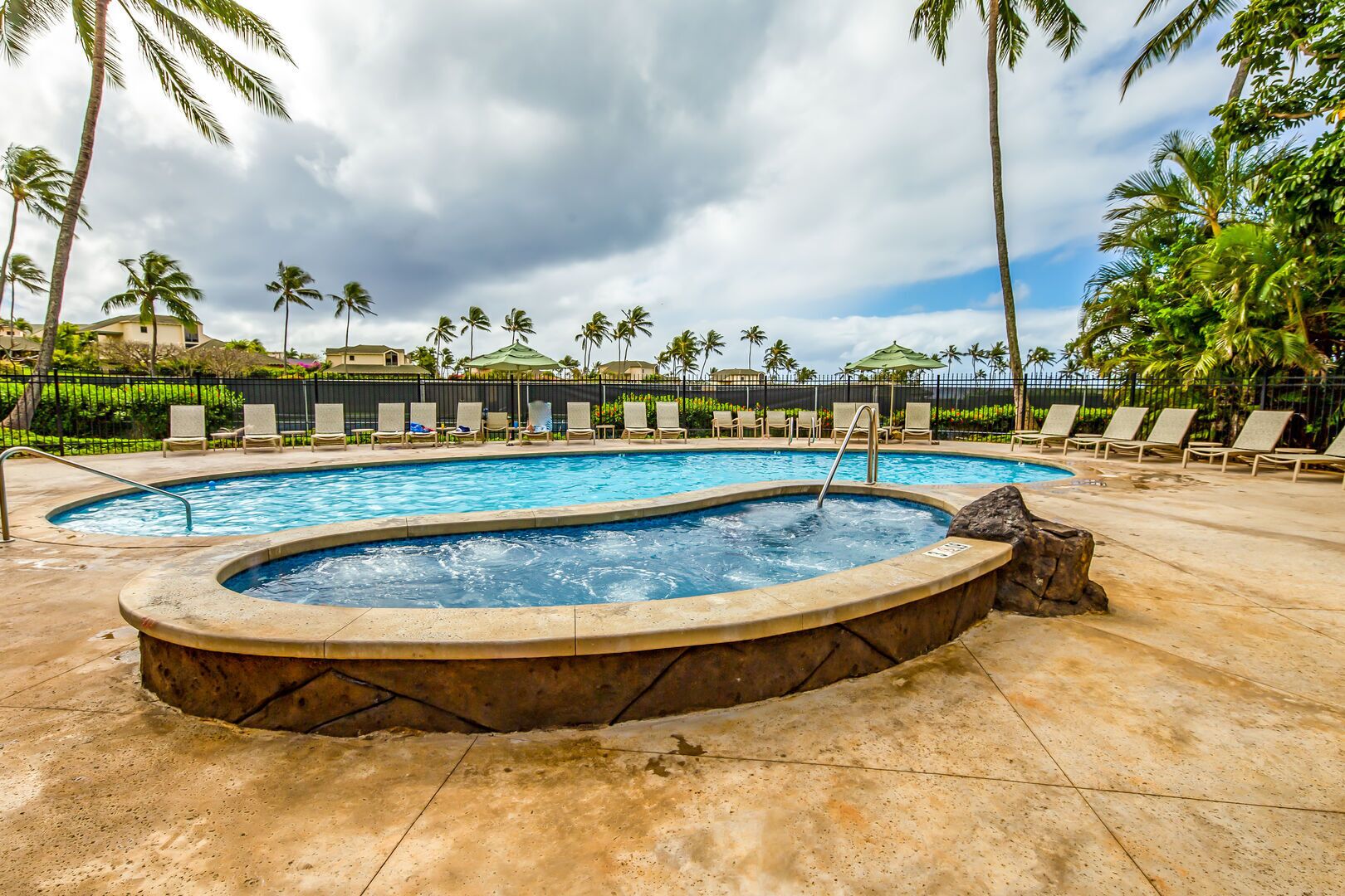 A swimming pool with a hot tub, surrounded by lounge chairs and palm trees.