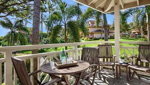 A covered outdoor seating area with wooden furniture, a table with a tray, and a bottle of water. - Regency Villas 120 - Luxury 3BR Poipu Kai Condo | Pool, Lanais & Central AC (Koloa)