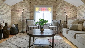 A cozy loft-style room with exposed brick walls, a large window with a stained glass design, a round wooden coffee table, and a comfortable sofa set. - Historic Top Floor Condo at the Grand Traverse Commons (Traverse City)