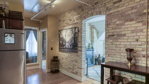 A kitchen with a brick wall, wooden flooring, and a stainless steel refrigerator. - Historic Top Floor Condo at the Grand Traverse Commons (Traverse City)