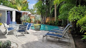 A poolside area with lounge chairs, a table, and a covered patio.