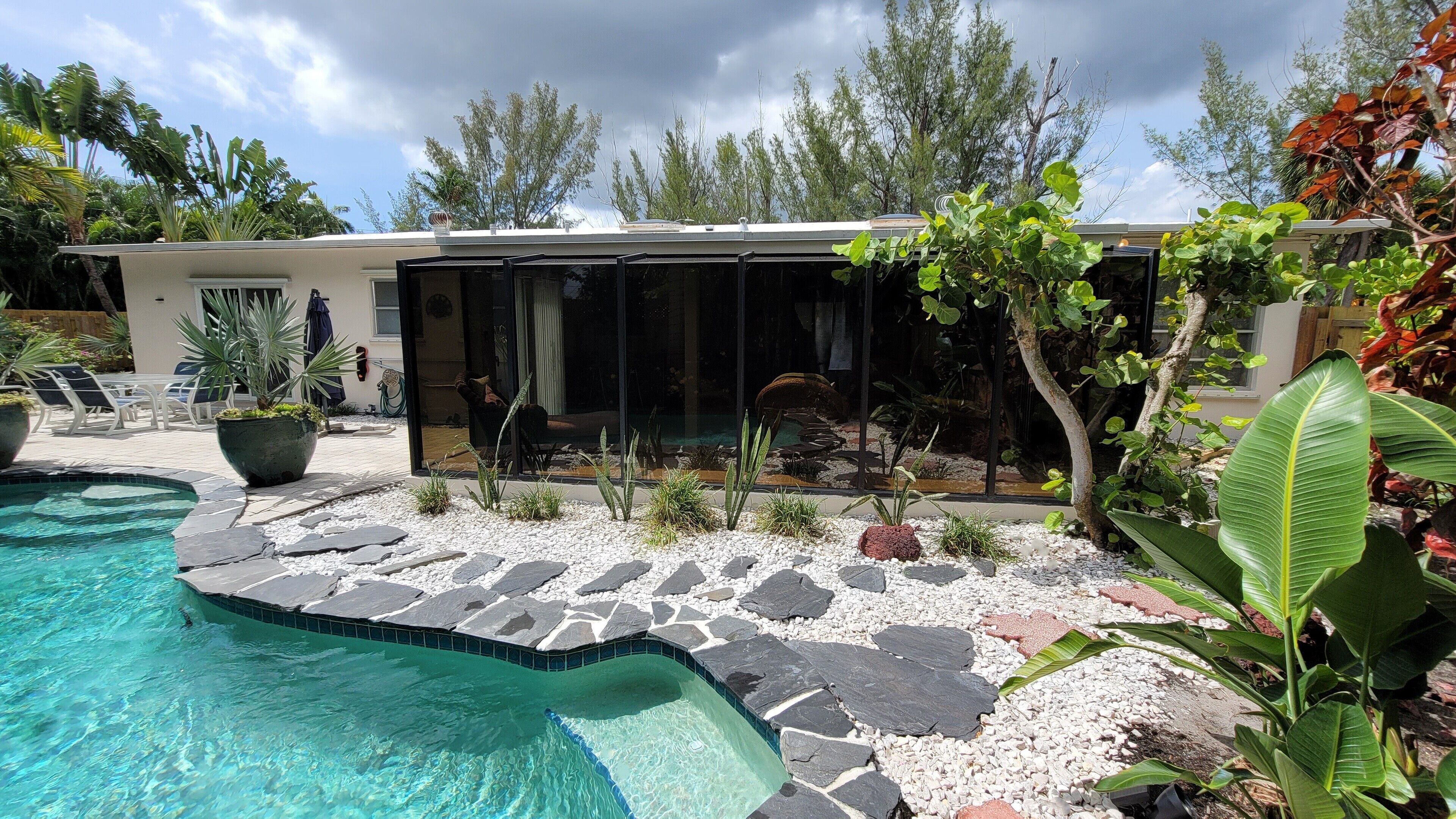 Uma casa moderna com piscina, rodeada por plantas tropicais e um caminho de pedra.