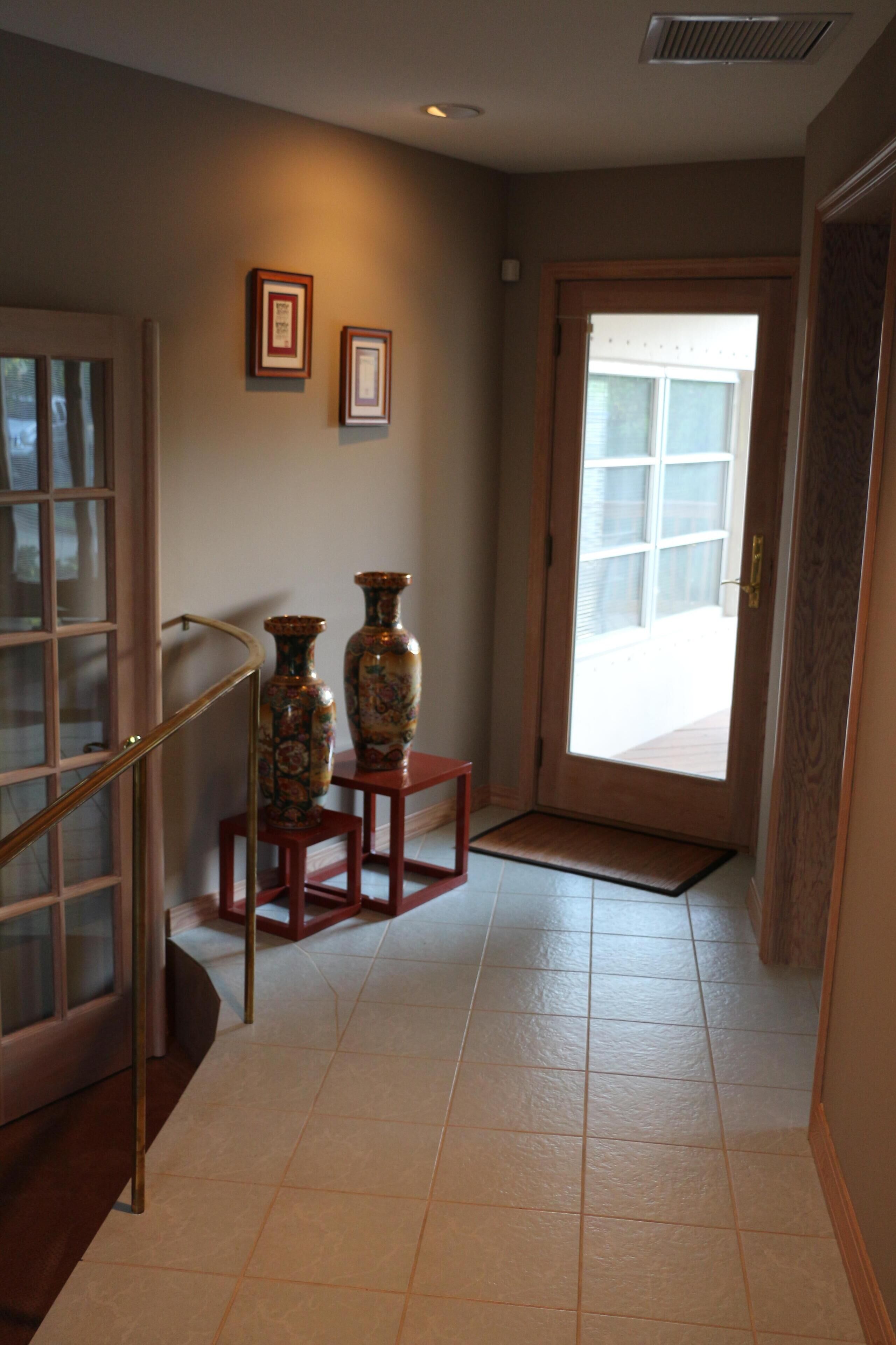 A hallway with a wooden door, a glass door, and two vases on a small table.