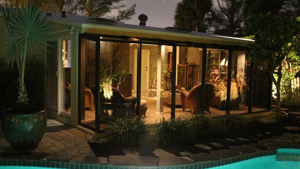 A glass-enclosed outdoor living area with a pool, surrounded by plants and furniture.