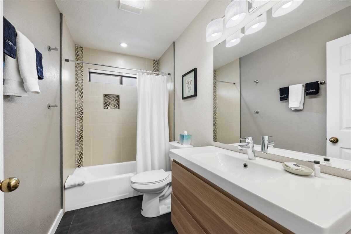 A modern bathroom with a large mirror, a bathtub, a toilet, and a vanity with a sink.