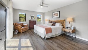Quarto com cama, sofá de couro, mesa de cabeceira e janela com vista para o verde.