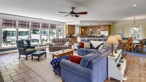 Ein geräumiges Wohnzimmer mit großem Sofa, Sesseln und Couchtisch. Es gibt einen Essbereich mit Tisch und Stühlen, und im Hintergrund eine Küche.
