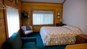 A cozy cabin room with a bed, a chair, a desk, and a window with curtains.