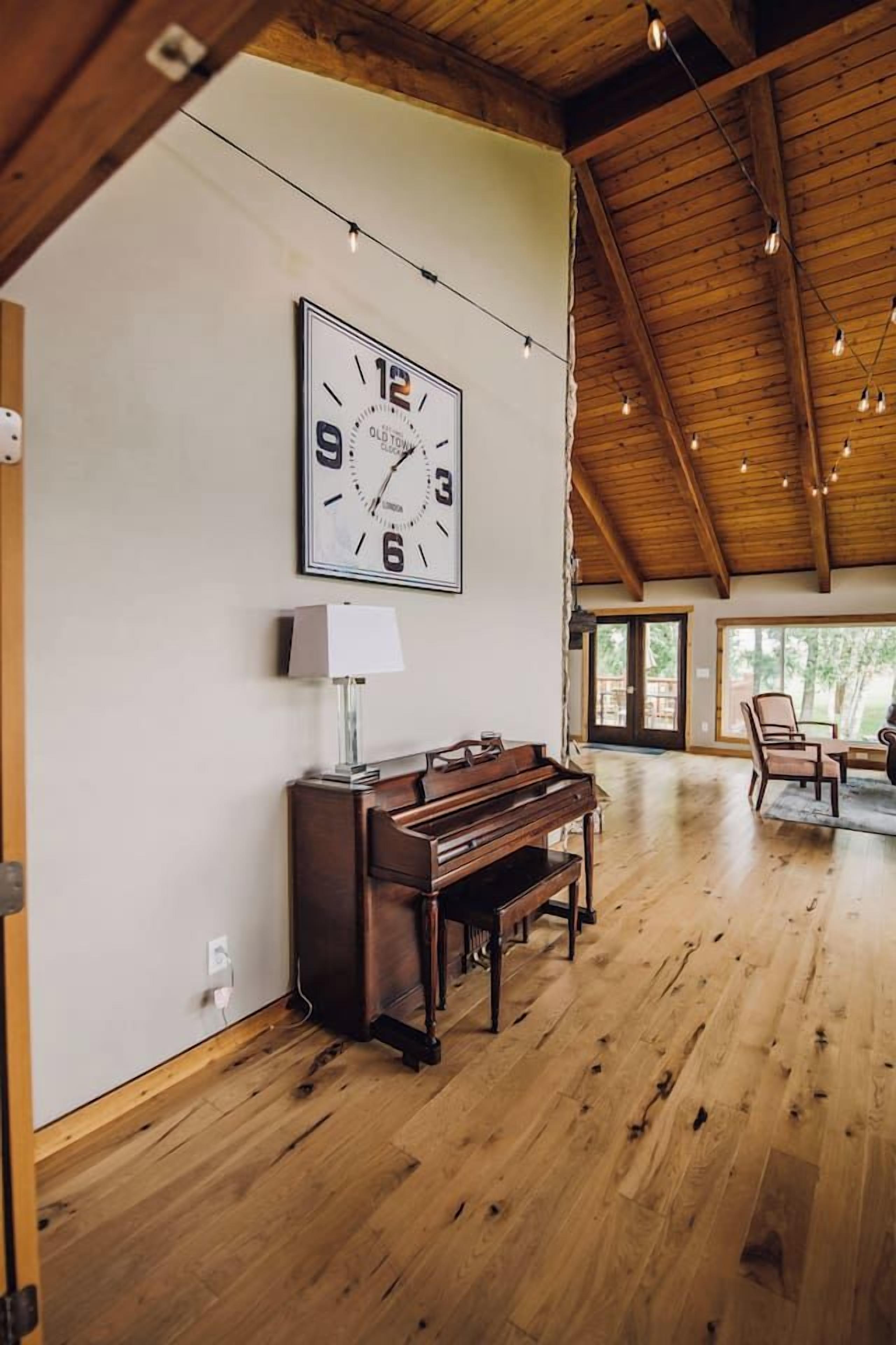 A spacious room with a wooden floor, a piano, a wall clock, and a door leading outside.