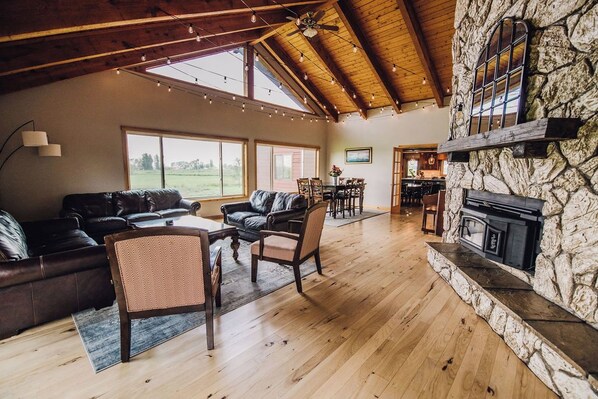 Amplia sala de estar con chimenea de piedra, muebles de cuero y ventanas grandes.
