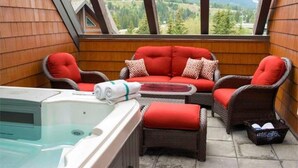 Uma varanda acolhedora com hidromassagem, móveis de vime e vista para as montanhas.