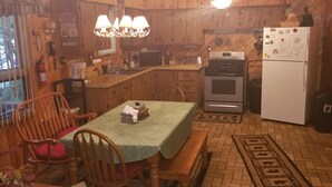 A compact kitchen with wooden cabinetry, a stove, a refrigerator, and a dining table with chairs. - Horsehead Lake Retreat (Big Discounts in June Call 414-378-7273)  (Presque Isle)